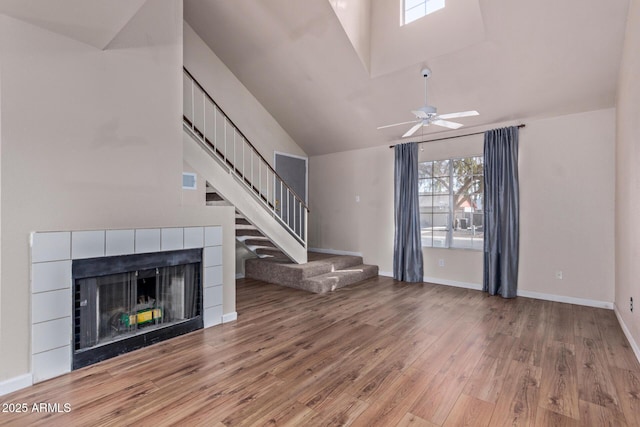 unfurnished living room with a tile fireplace, high vaulted ceiling, ceiling fan, and light wood-type flooring