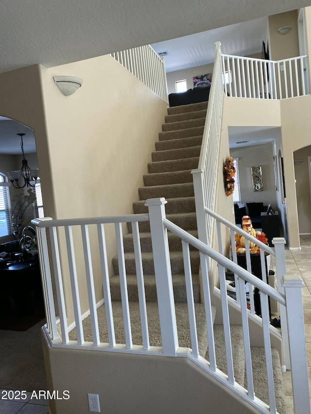 stairs with tile patterned flooring, a towering ceiling, and a chandelier