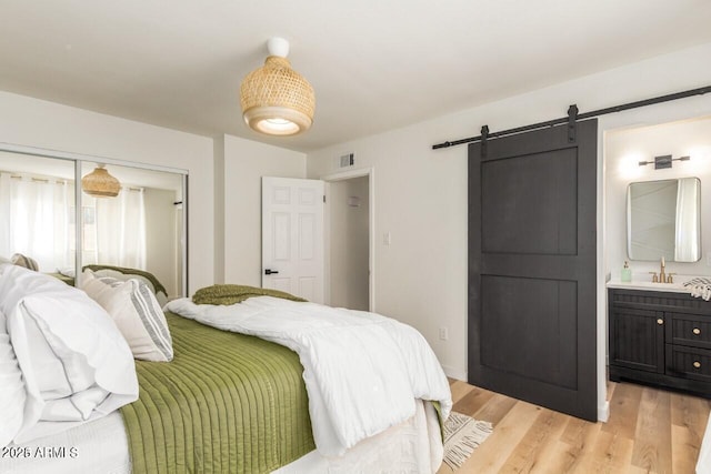 bedroom with sink, light wood-type flooring, a barn door, ensuite bath, and a closet