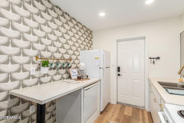 kitchen with white cabinetry, sink, white appliances, and light hardwood / wood-style floors