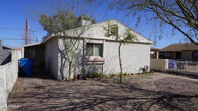 view of side of home with stucco siding, a chimney, and fence