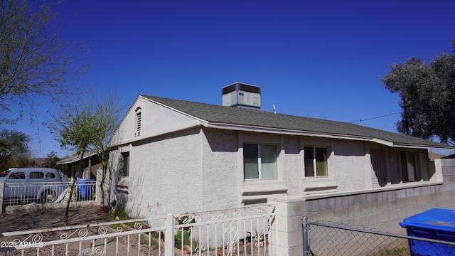 view of side of home with stucco siding, a shingled roof, and fence