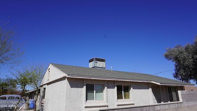 view of home's exterior featuring a shingled roof, central air condition unit, fence, and stucco siding