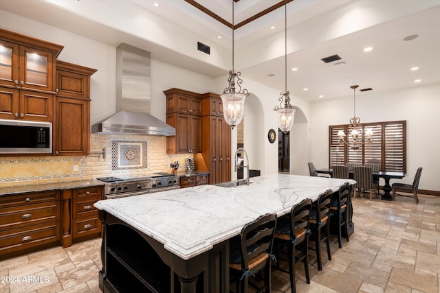 kitchen featuring tasteful backsplash, wall chimney range hood, hanging light fixtures, built in microwave, and a large island