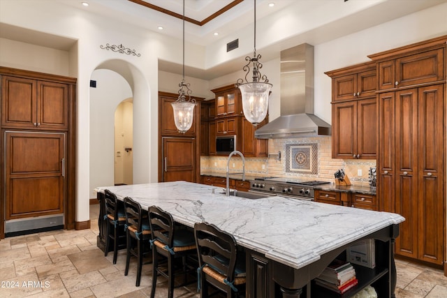 kitchen featuring sink, decorative backsplash, wall chimney range hood, and a spacious island