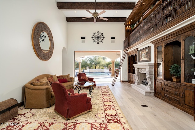 living room featuring a high ceiling, ceiling fan, light hardwood / wood-style flooring, and beamed ceiling