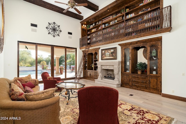 living room with light hardwood / wood-style floors, ceiling fan, beam ceiling, and a towering ceiling