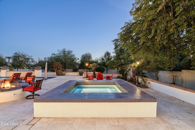 pool at dusk featuring an outdoor fire pit, a patio area, and an in ground hot tub