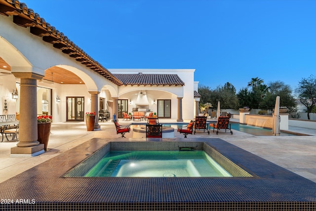 pool at dusk with an in ground hot tub and a patio