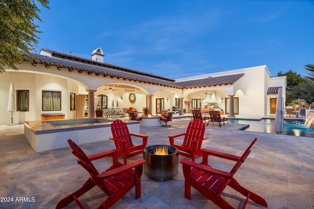 patio terrace at dusk featuring a pool with hot tub, an outdoor fire pit, ceiling fan, and an outdoor bar