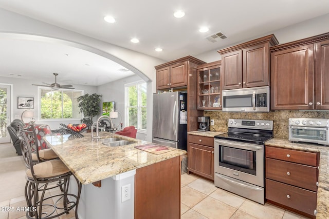 905 S Osborn Ln, Gilbert, AZ 85296 - kitchen with stainless steel appliances, arched walkways, a breakfast bar, light stone counters, and light tile patterned floors