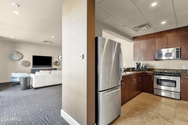 kitchen with dark stone countertops, dark brown cabinetry, light tile floors, and stainless steel appliances