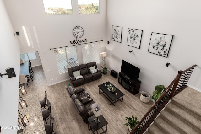 living area with a towering ceiling, baseboards, stairway, and wood finished floors