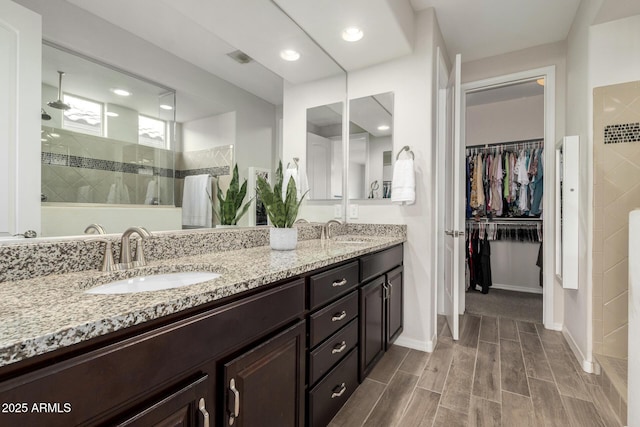 full bathroom featuring a walk in closet, double vanity, a sink, and a walk in shower