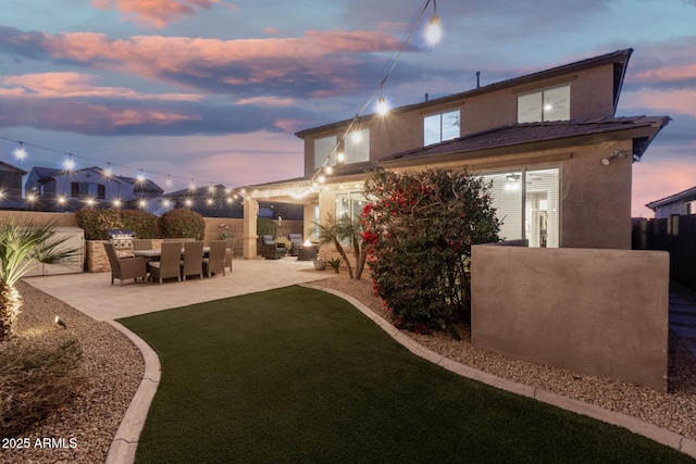 back of property at dusk with a patio, an outdoor kitchen, fence, and stucco siding