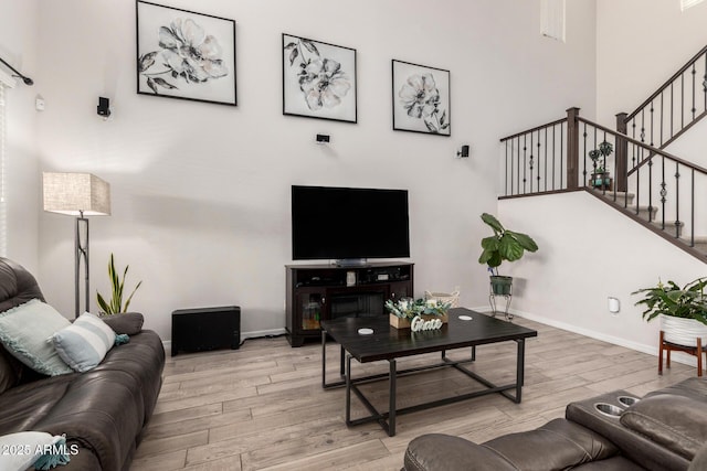 living room featuring a high ceiling, stairs, baseboards, and wood finished floors