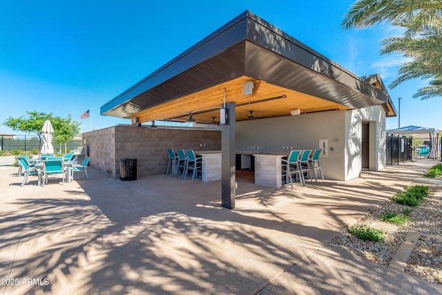 exterior space with a ceiling fan, outdoor dry bar, fence, a patio area, and stucco siding