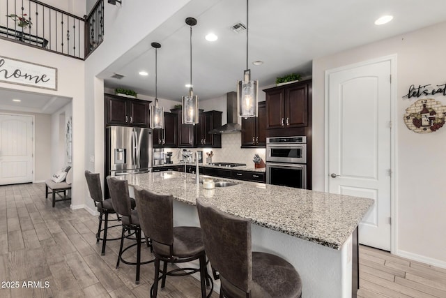 kitchen featuring dark brown cabinetry, visible vents, wood tiled floor, stainless steel appliances, and wall chimney range hood