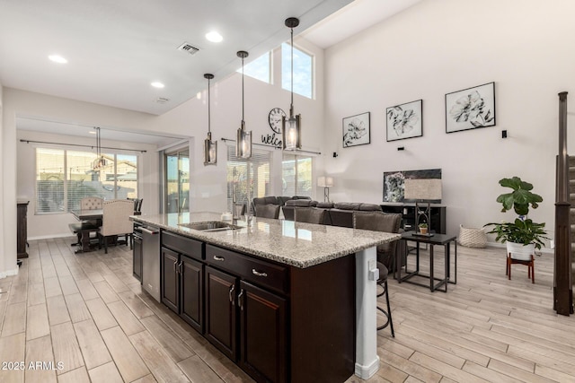 kitchen featuring wood tiled floor, a kitchen island with sink, visible vents, and a breakfast bar area