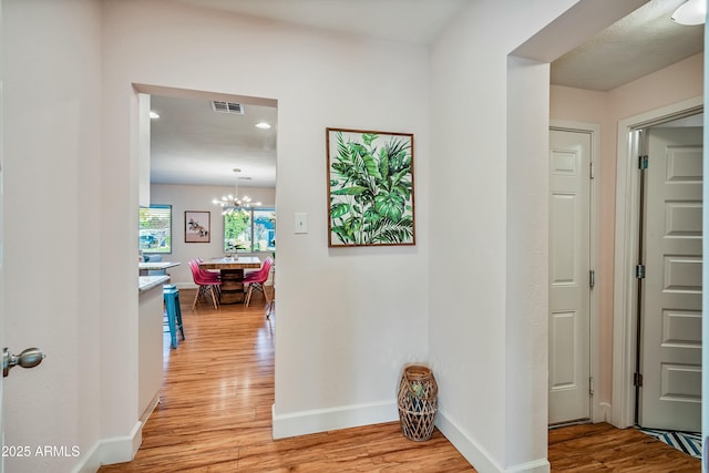 corridor with light hardwood / wood-style floors and a chandelier