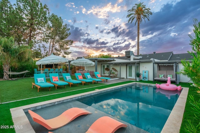 pool at dusk featuring central AC unit and a yard