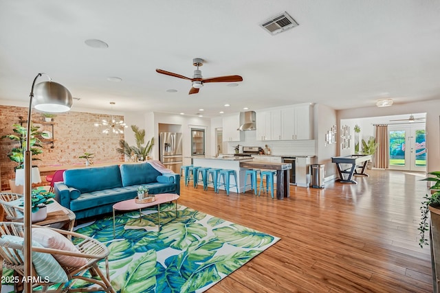 living room featuring ceiling fan with notable chandelier, french doors, sink, and light hardwood / wood-style flooring