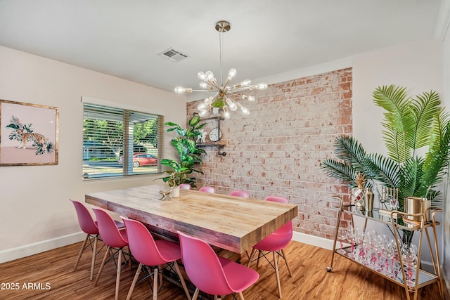 dining room featuring brick wall, a notable chandelier, and hardwood / wood-style flooring