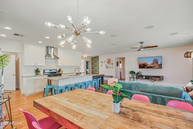 dining space featuring ceiling fan with notable chandelier, light hardwood / wood-style floors, and sink