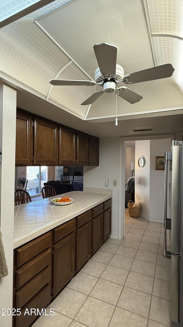 kitchen with stainless steel refrigerator, ceiling fan, dark brown cabinets, tile counters, and light tile patterned flooring