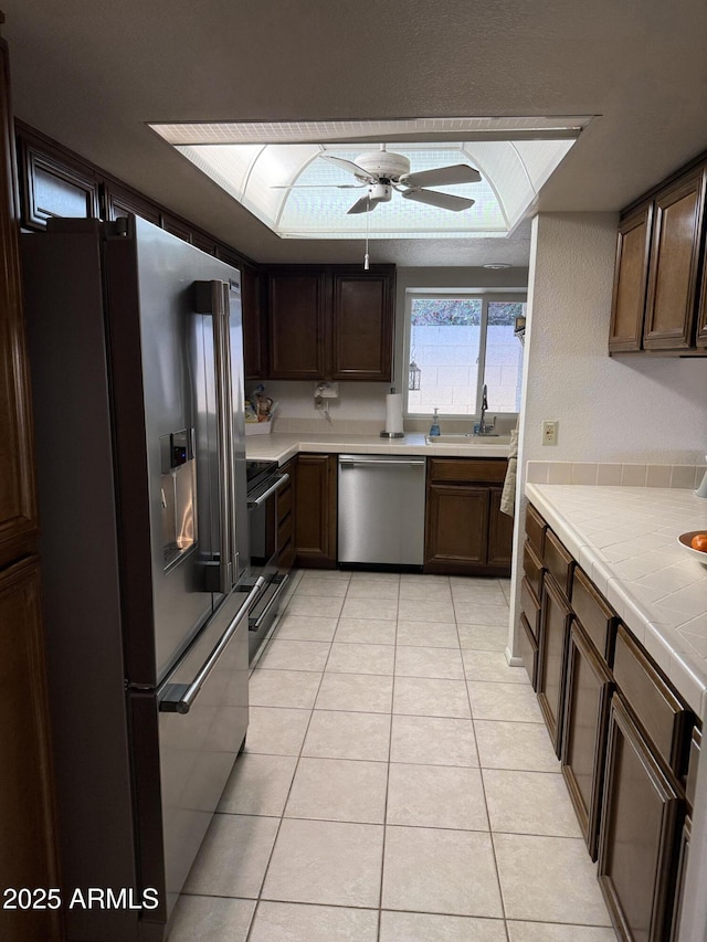 kitchen with sink, light tile patterned floors, tile counters, ceiling fan, and stainless steel appliances