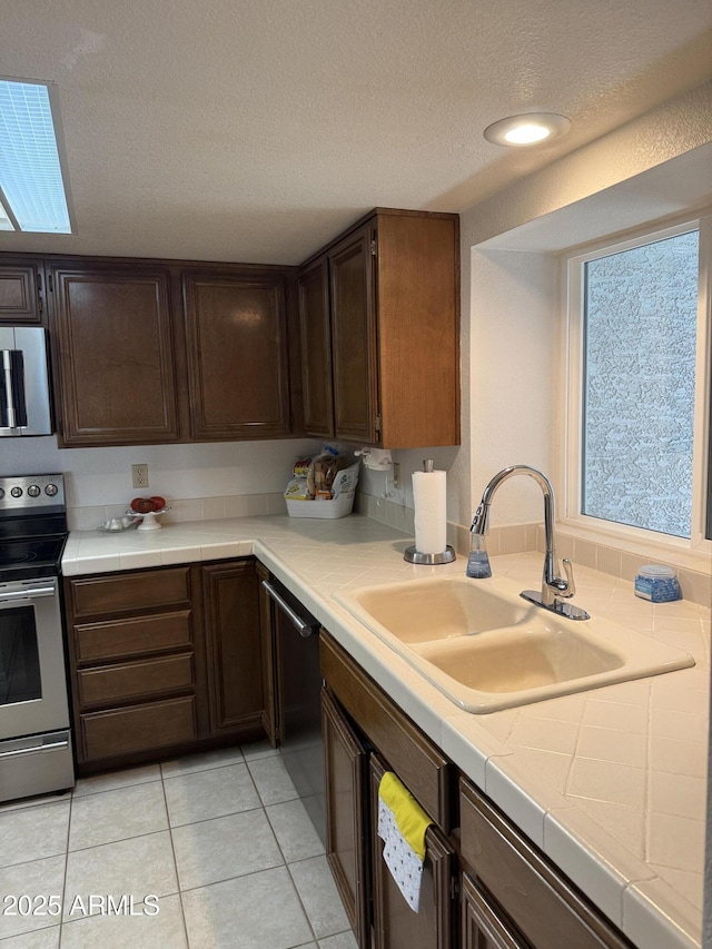 kitchen with dishwasher, sink, stainless steel range with electric cooktop, dark brown cabinetry, and a textured ceiling