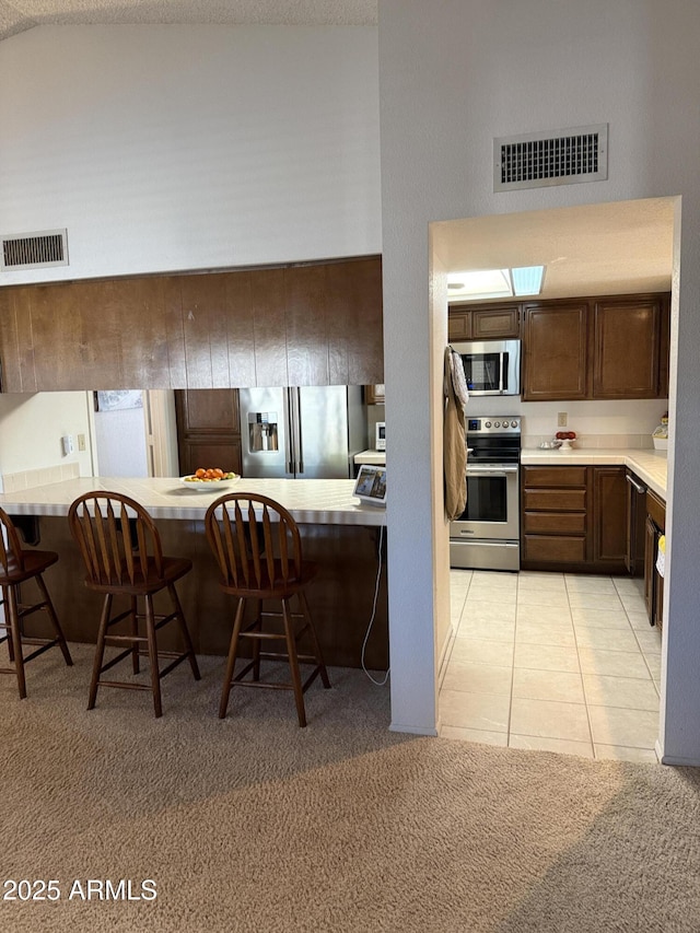 kitchen with a high ceiling, light tile patterned flooring, appliances with stainless steel finishes, and a breakfast bar area