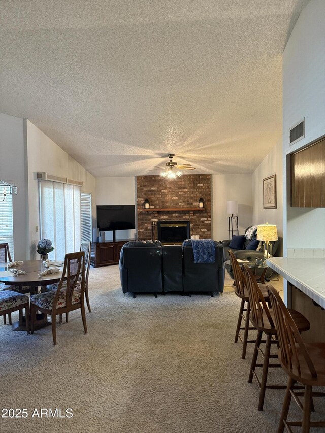 dining area featuring vaulted ceiling, light carpet, a textured ceiling, ceiling fan, and a fireplace