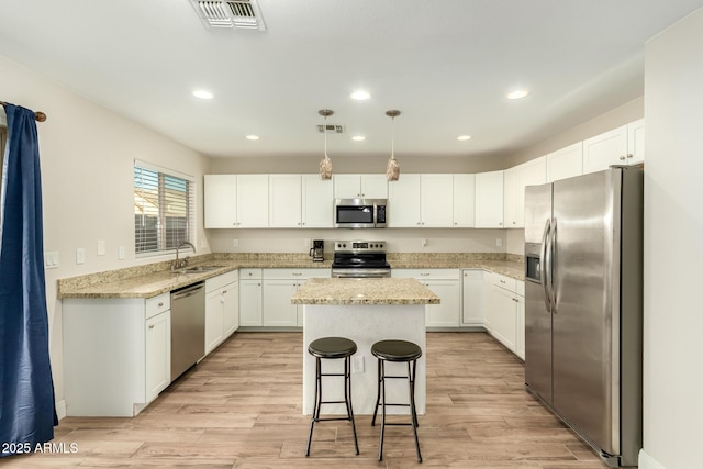 kitchen featuring appliances with stainless steel finishes, a kitchen island, decorative light fixtures, white cabinetry, and sink