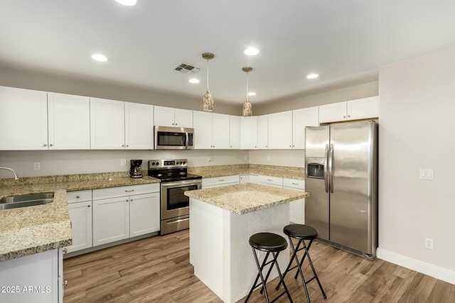 kitchen featuring white cabinetry, stainless steel appliances, decorative light fixtures, a kitchen island, and sink