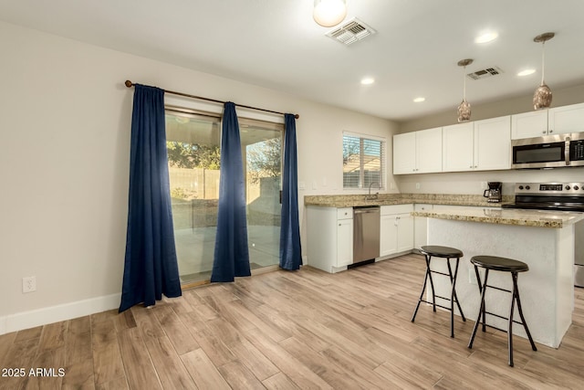 kitchen featuring light stone counters, white cabinets, appliances with stainless steel finishes, and light wood-type flooring