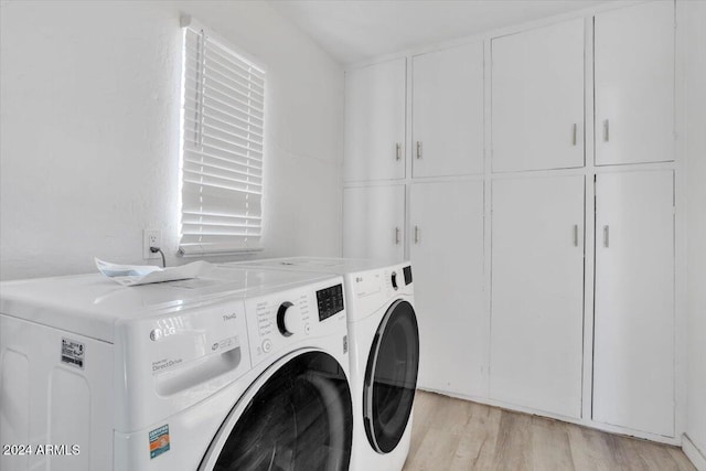 laundry room with washing machine and clothes dryer, cabinets, and light wood-type flooring