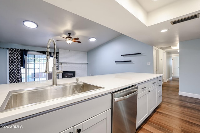 kitchen featuring white cabinetry, sink, a brick fireplace, stainless steel dishwasher, and hardwood / wood-style floors