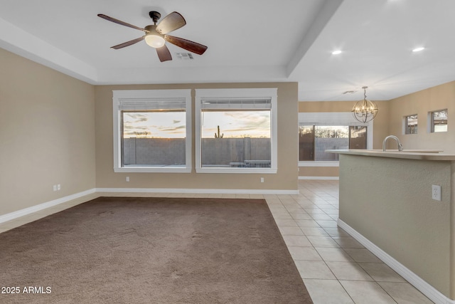 spare room with light tile patterned floors, ceiling fan with notable chandelier, and a raised ceiling