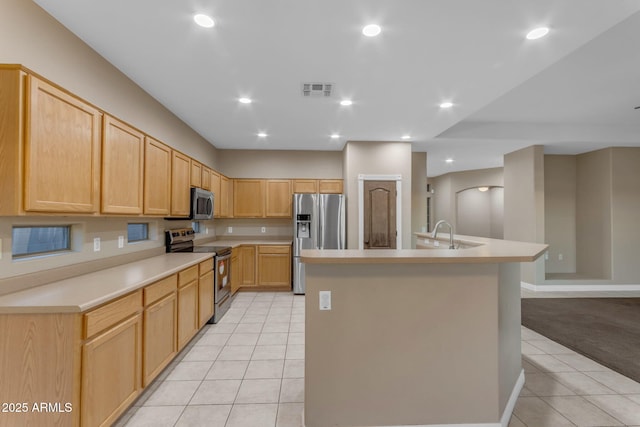 kitchen featuring an island with sink, appliances with stainless steel finishes, light tile patterned flooring, and light brown cabinetry