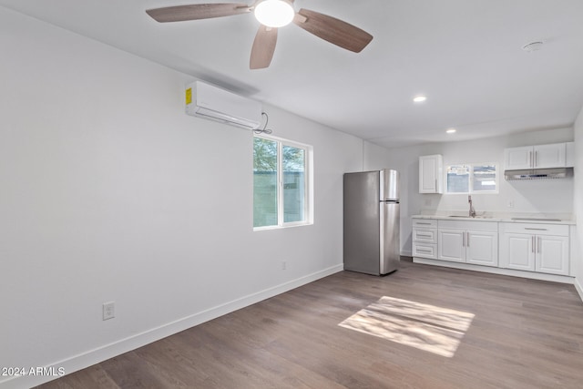 kitchen featuring white cabinets, a wall unit AC, stainless steel refrigerator, and light hardwood / wood-style flooring