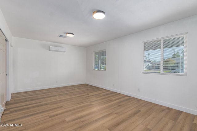 unfurnished room featuring a wall mounted air conditioner, visible vents, baseboards, and light wood finished floors