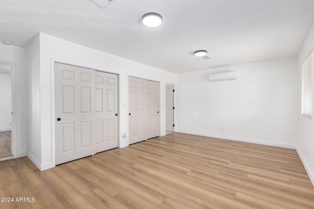 unfurnished bedroom with baseboards, multiple closets, light wood-style floors, and an AC wall unit