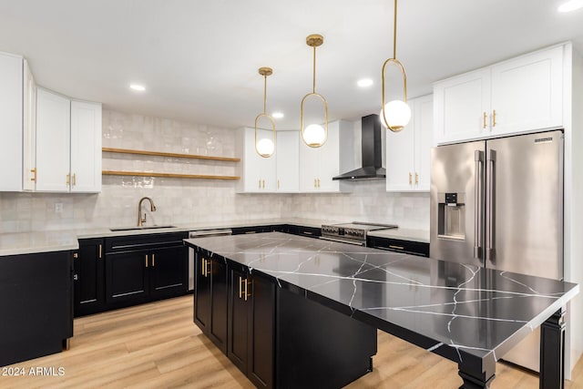 kitchen with a sink, a kitchen island, stainless steel appliances, wall chimney exhaust hood, and dark cabinets