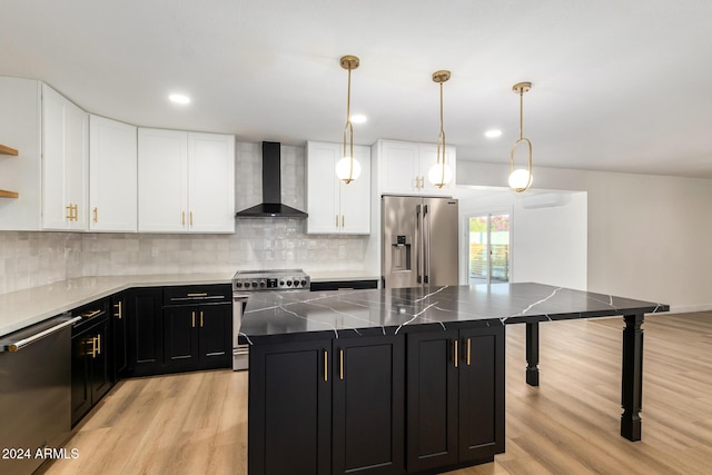 kitchen with wall chimney range hood, appliances with stainless steel finishes, dark cabinetry, light wood-style floors, and white cabinets