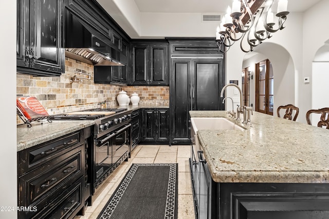 kitchen with light stone countertops, sink, wall chimney range hood, an island with sink, and high end appliances