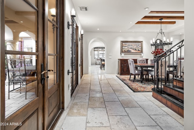 hall with french doors, a healthy amount of sunlight, a chandelier, and a raised ceiling