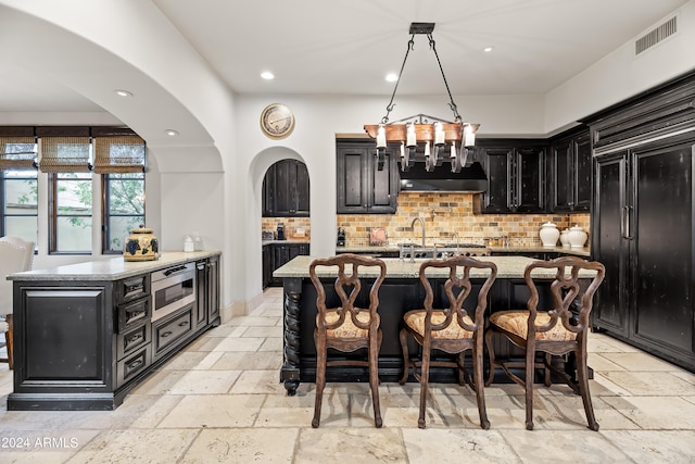 kitchen with a center island with sink, a kitchen breakfast bar, light stone counters, and pendant lighting