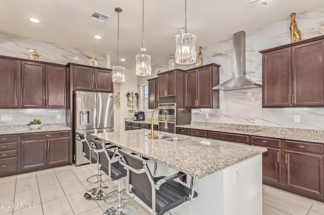 5218 N Tiller Dr, Litchfield Park, AZ 85340 - kitchen featuring stainless steel appliances, wall chimney exhaust hood, a sink, light stone counters, and a center island with sink