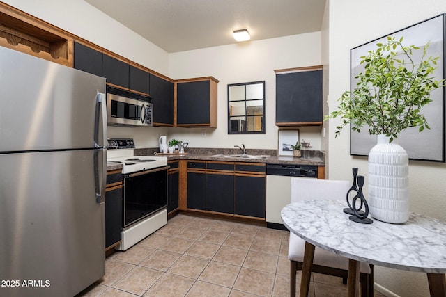 kitchen with light tile patterned flooring, stainless steel appliances, a sink, dark cabinetry, and dark countertops